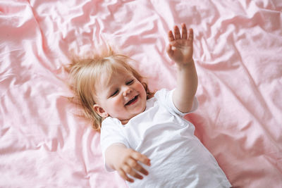 Cute funny baby girl child in white clothes on bed at home, view from top