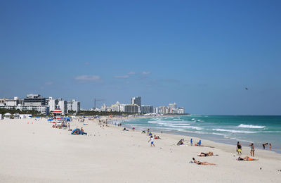 People at beach against blue sky during sunny day