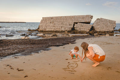 Mother and daughter drawing on sand at beach