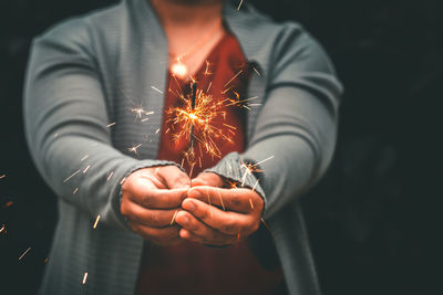 Midsection of woman holding illuminated sparkler against black background