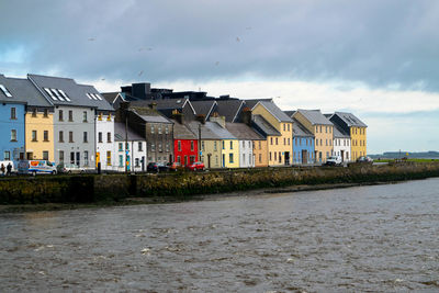 Houses by river and buildings against sky