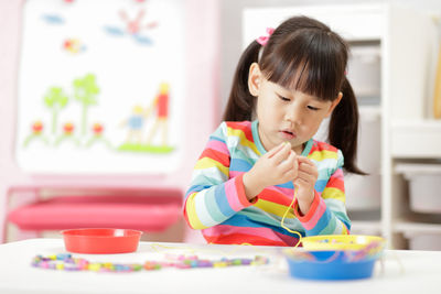 Girl playing with beads and string at home