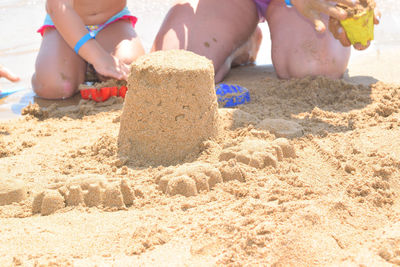 Low section of children by sandcastle at beach