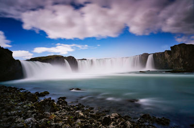 Scenic view of waterfall against cloudy sky