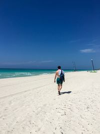 Rear view of man walking on beach against clear blue sky