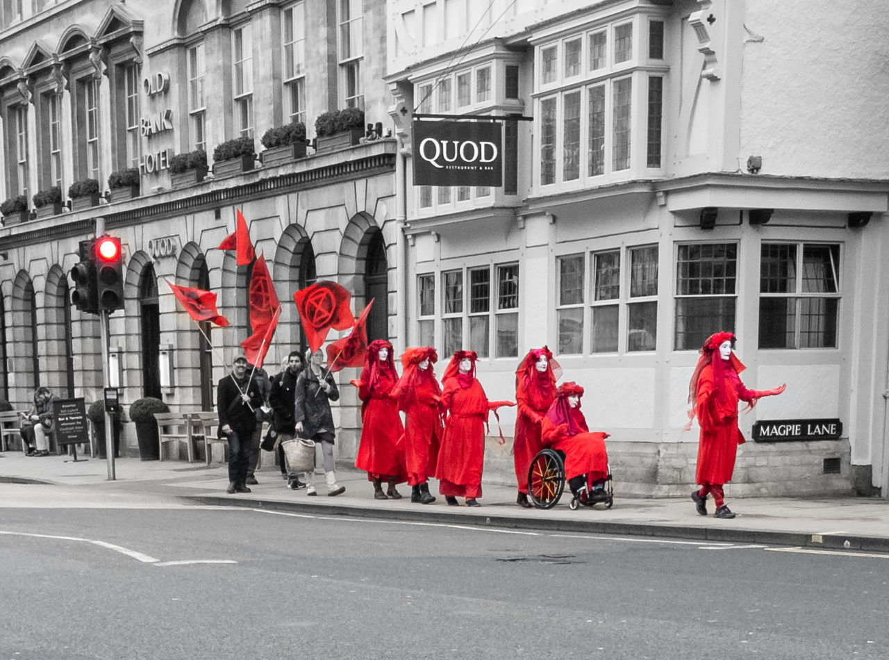 architecture, city, building exterior, group of people, street, road, built structure, men, crowd, red, women, day, clothing, uniform, government, adult, transportation, walking, sign, large group of people, celebration, city street, outdoors, full length, city life