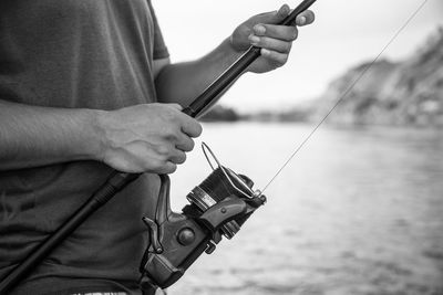 Close-up of man holding fishing rod by water