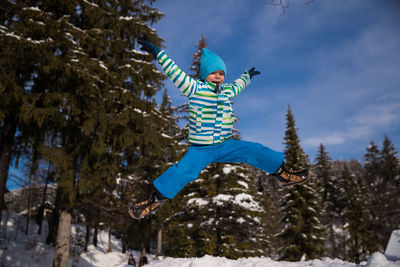 Boy jumping in snow against sky