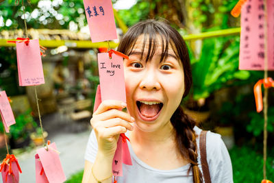 Portrait of excited woman holding paper with text while standing outdoors