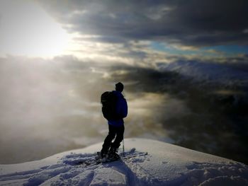 Rear view of man standing on snowcapped mountain against cloudy sky