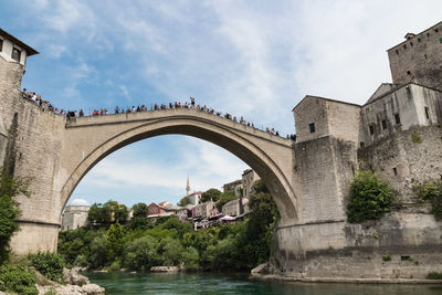 Arch bridge over river by buildings against sky