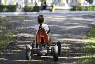 A girl in the park rides a four-wheeled bicycle