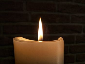 Close-up of lit candle against wall