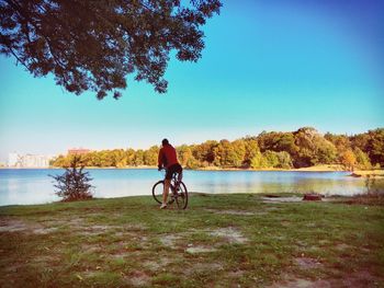 Man with bicycle on lakeshore against clear sky