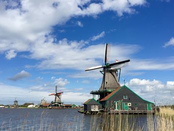 Windmills by river against cloudy sky