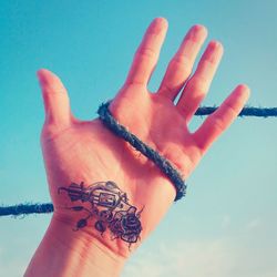 Cropped image of person with tattoo on hand against sky