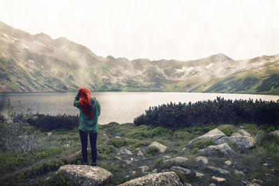 Rear view of woman standing on rock by lake against clear sky