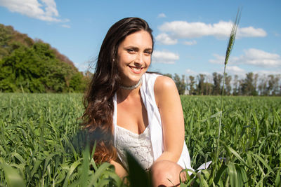 Portrait of young woman sitting on field against sky