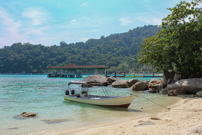 Boats moored on sea by trees against sky