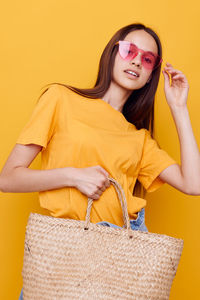 Portrait of teenager girl holding bag against yellow background