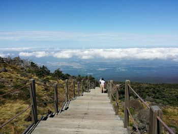 Rear view of woman walking on footbridge by sea against sky