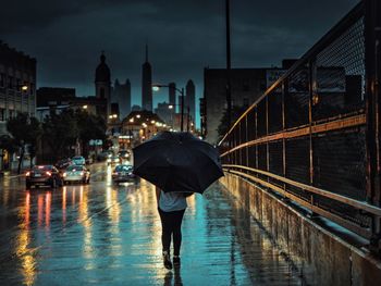 Rear view of woman walking on city street at dusk during rainy season