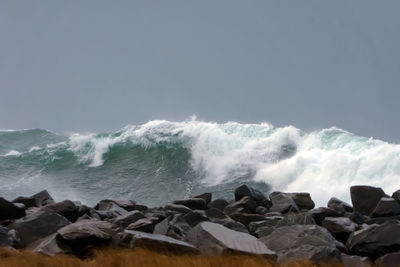 Waves splashing on rocks at shore against sky