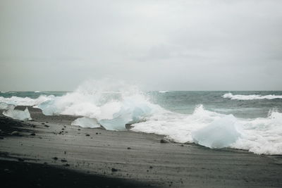 Waves breaking on beach against sky