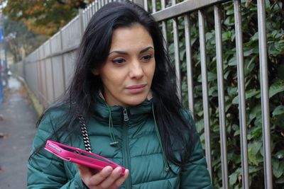 Close-up of beautiful young woman with smart phone standing on footpath