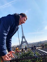 Optical illusion of man eating eiffel tower against sky in city