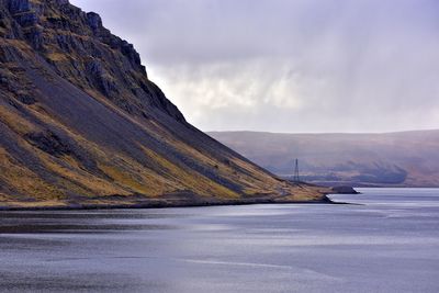 Scenic view of sea by mountains against cloudy sky