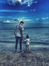 Rear view of father and son at beach against sky