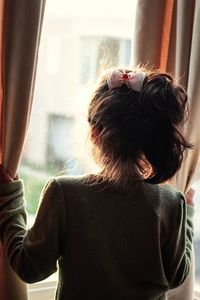 Rear view of girl looking through window while standing at home