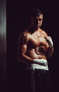 Portrait of shirtless male athlete wearing hand wrap while standing in darkroom