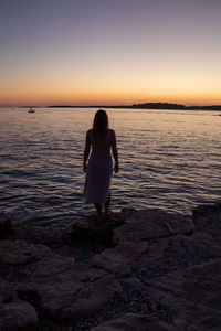 Rear view of woman standing on beach during sunset