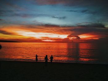 Silhouette people standing on beach against sky during sunset