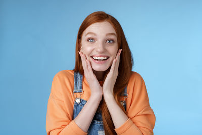 Excited woman touching face against blue background