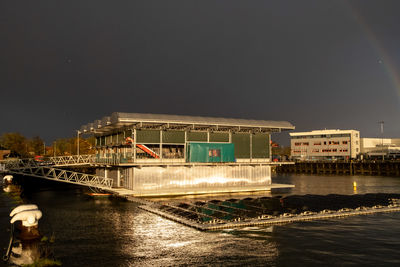 Illuminated bridge over river by buildings against sky at night