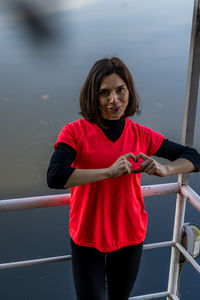 Portrait of smiling woman making heart shape by railing