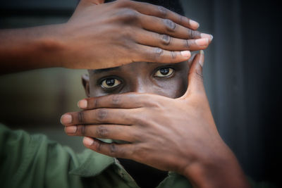 Portrait of young black skin man with hands cover his face standing against wooden door.