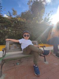 Portrait of boy sitting on tree against plants