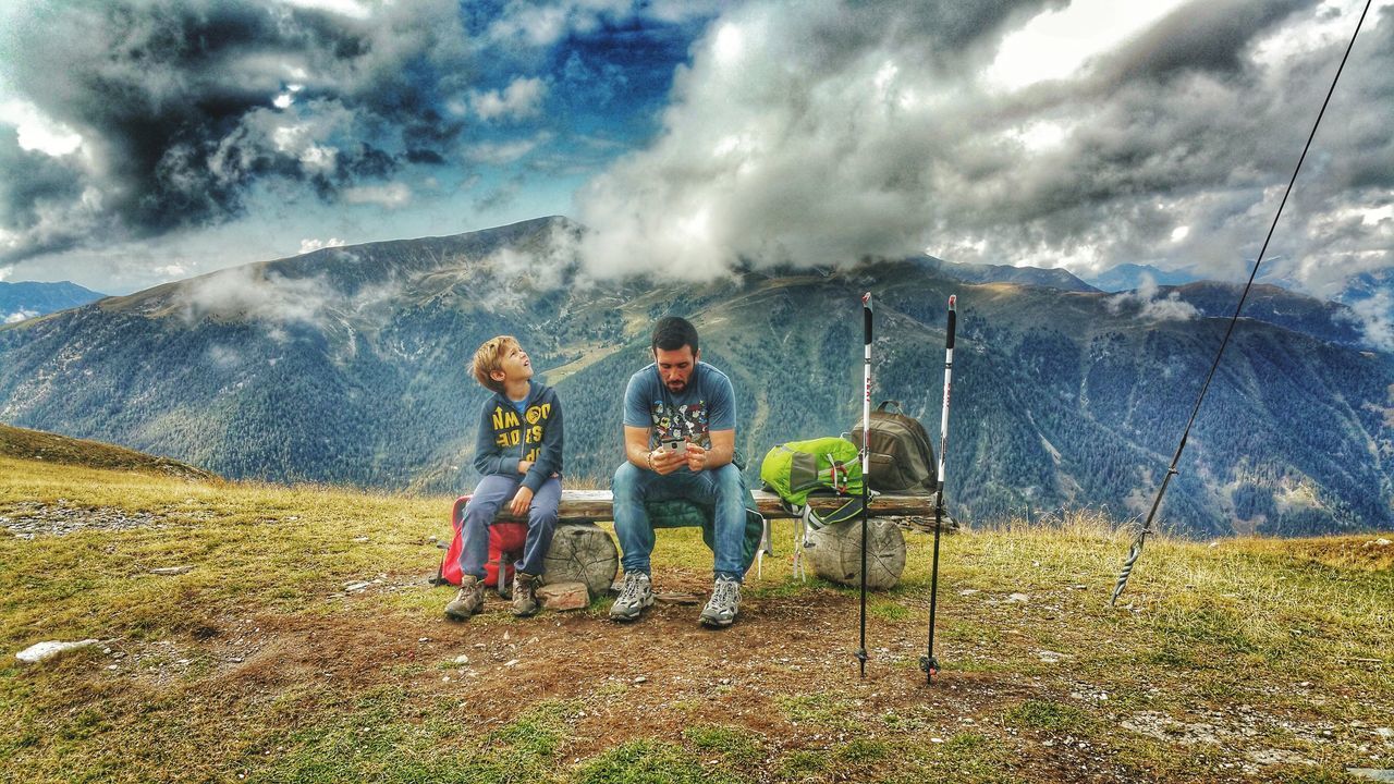 COUPLE SITTING ON MOUNTAIN AGAINST SKY