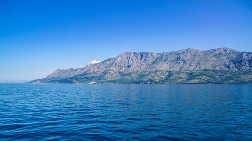 Scenic view of sea and mountains against clear blue sky