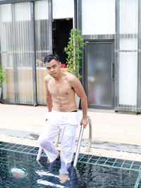 Portrait of young man standing by swimming pool