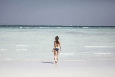 Full length rear view of woman in biking walking towards sea against clear sky