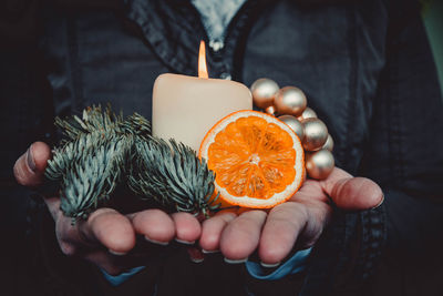 Midsection of person holding burning candle and decorations