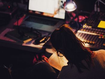 Rear view of woman reading book while sitting by sound mixer in studio 