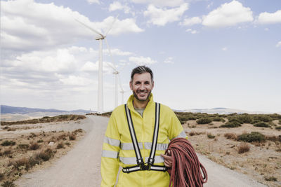 Smiling technician with rope standing at wind farm