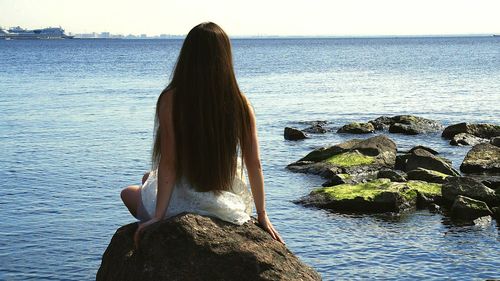 Rear view of woman standing on rock by sea against clear sky