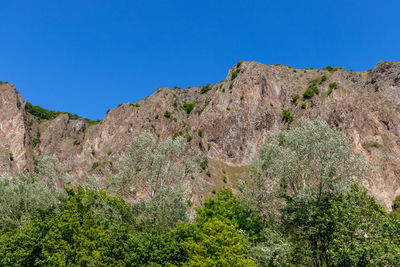 Low angle view of rocky mountains against clear blue sky
